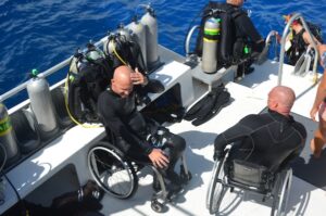 Two adaptive divers in wheelchairs on a boat deck